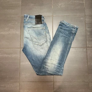 Replay - Säljer ett par ljusblå Replay Anbass jeans med snygga slitningar och tvättade detaljer. Klassisk femficksmodell med normal passform och raka ben. Perfekta för dig som gillar en avslappnad men stilren look.
