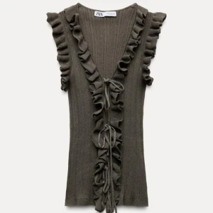 Brun ribbad topp med volang från Zara - Supersnygg brun ribbad topp från Zara med volangdetaljer längs ärmhålen och framtill. Djup v-ringning och knyt framtill ger en trendig look. Perfekt att styla med jeans eller kjol.