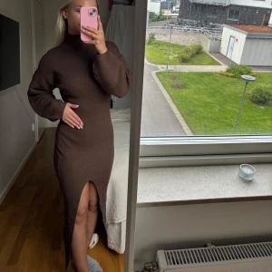 Brun ribbad långklänning med slits - Säljer en brun ribbad långklänning med hög hals och lång ärm. Klänningen har en snygg slits framtill som ger en modern touch. Perfekt för dig som gillar en tight passform och stickat material.