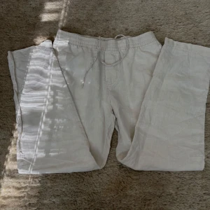 Vita linnebyxor från H&M - Säljer ett par vita linnebyxor från H&M med regular fit. Byxorna har resår i midjan. Perfekta för varma dagar och har en avslappnad, rak siluett.
