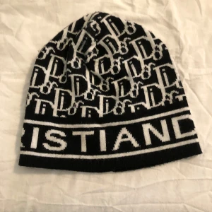Svartvit mössa från Dior - Snygg svartvit mössa från Dior med tydlig logotyp och mönster av bokstäver. Tillverkad i bomull och akryl, perfekt för att ge din outfit en exklusiv touch. Mjuk och bekväm passform. Den är äkta och endast använd ett par gånger säljs endast för 249 kr denna vecka sedan är priset 499 kr igen så passa på och köp!