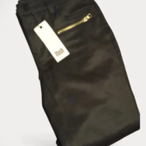 Svarta byxor med guldfärgad dragkedja - Snygga svarta byxor med en guldfärgad dragkedja framtill. Byxorna har en klassisk passform och är perfekta för dig som vill ha en stilren look med en liten detalj. Märkeslapp sitter kvar.