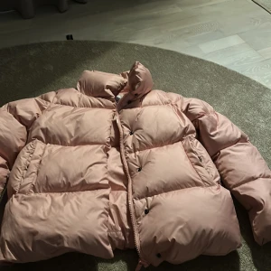 Ljusrosa pufferjacka från Tommy Hilfiger - Säljer en ljusrosa pufferjacka från Tommy Hilfiger. Jackan har hög krage, stora vadderade partier och dragkedja framtill. Perfekt för kyligare dagar och riktigt snygg färg som sticker ut.