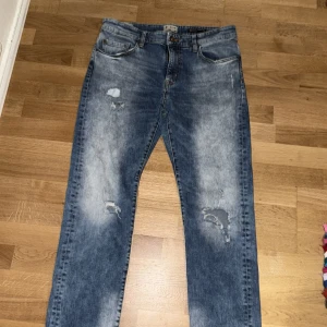 Blå slim jeans - Säljer ett par blå slim fit jeans med slitna ben för att få till en street look. Helt oanvända. Storlek 36. Perfekt till sommaren. Säljer då den är lite för korta för mig vid bena.
