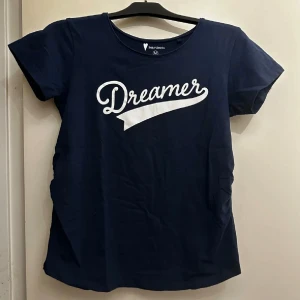 Mörkblå t-shirt med tryck - Mörkblå t-shirt med vit text 'Dreamer' tryckt på bröstet. Klassisk rund halsringning och korta ärmar. Aldrig använd.