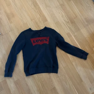 Mörkblå sweatshirt från Levi's - Säljer en mörkblå sweatshirt från Levi's med klassisk röd logga framtill. Tröjan har rund halsringning och långa ärmar. Perfekt för en avslappnad och stilren look.