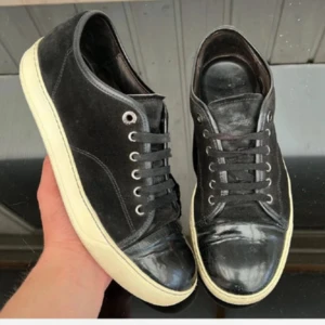 Lanvin - Säljer ett par svarta sneakers från Lanvin med vit, platt sula. Skorna har snörning, rund tå och en kombination av mocka och skinn på ovandelen. Klassisk och stilren design med metallfärgade öljetter och diskret sömnad.uk6 motsvarar 40-41! Skick 7/10! 