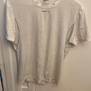 Vit funktions-t-shirt från Craft - Säljer en vit funktions-t-shirt från Craft i storlek M. T-shirten är tillverkad i polyester och lycra, har korta ärmar och meshpaneler för extra ventilation. Perfekt för träning eller löpning. Enkel och sportig design med Craft-logga på bröstet.
