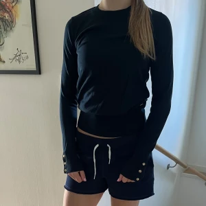 Mörkblå tröja med gulddetaljer från Holly & Whyte - Säljer en mörkblå långärmad tröja från Holly & Whyte by Lindex. Tröjan har ribbade muddar med snygga guldfärgade knappar vid ärmsluten och rund halsringning. Perfekt till många olika outfits!