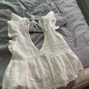 Vit volangtopp från Nelly - Säljer en söt vit topp från Nelly i storlek 34. Toppen har volangdetaljer vid axlarna, v-ringning och knytning i ryggen. Tillverkad i ett lätt och luftigt bomullsliknande material, perfekt för varma dagar. Skriv om ni har nå frågor❤️