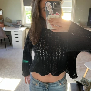 Svart stickad croppad tröja - Säljer en svart stickad croppad tröja med hålmönster. Tröjan har långa ärmar och en lös passform med vågig nederkant. Perfekt att styla med jeans eller kjol för en trendig look.