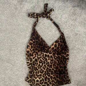 Leopardmönstrad halterneck topp - Säljer en leopardmönstrad halterneck topp med knyt i nacken. Toppen har djup v-ringning och är figurnära i modellen. Perfekt för dig som vill sticka ut med ett djuriskt mönster.