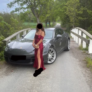 Vinröd axelbandslös långklänning med slits - Säljer en vinröd axelbandslös långklänning med hög slits och figurnära passform. Klänningen har en elegant omlott-detalj och är perfekt för festliga tillfällen. Materialet har en lätt glansig finish som ger en lyxig känsla.