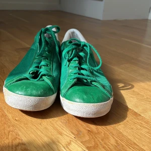 Gröna Rod Laver sneakers från Adidas - Säljer ett par gröna Adidas Rod Laver sneakers med vit sula och vita detaljer vid hälen. Skorna har snörning och är tillverkade i syntetmaterial med meshstruktur för extra ventilation. Klassisk och sportig modell med låg profil. Har lite smä fläckar och jag kan förhändla pris