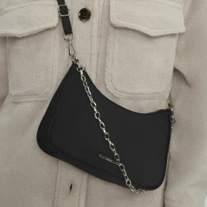 Svart axelväska med kedjedetalj - Snygg svart axelväska med en cool kedjedetalj och justerbar axelrem. Väskan har en dragkedja för säker förvaring och en stilren design som passar perfekt till olika outfits. Inte använd!