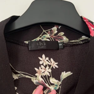 Svart blommig klänning från SHK Paris - Säljer denna blommiga klänning som egentligen är en byxdress – ser ut som en klänning men har shorts undertill. Perfekt för en varm sommardag! Obs: saknar midjebandet🌸🌸