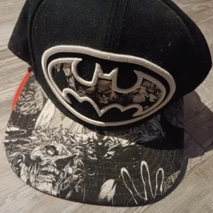 Svart Batman-keps med tryck - Snygg svart keps med Batman-logga i vitt och detaljerat tryck på skärmen. Perfekt för fans av serietidningar och superhjältar. Justerbar passform för bekvämlighet. Samt en top keps