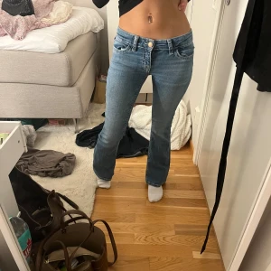 Blå jeans från Gina Tricot - Snygga blå jeans från Gina Tricot med låg midja och bootcut-stil. De har en klassisk femficksdesign och en knappdetalj på bakfickan. Perfekta för en avslappnad look. Är i storlek 152 men är som xs-xxs.