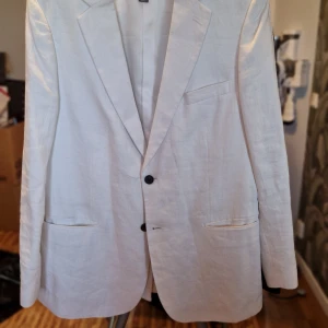 Vit kavaj - Elegant vit kavaj med klassisk design och två knappar framtill. Perfekt för sommarens festligheter. Tillverkad i ett lätt och bekvämt material.