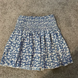 Kjol  - Charmig blå kjol med blommigt mönster från Shein. Kjolen har en elastisk midja och volangdetaljer som ger en lekfull look. Perfekt för varma dagar och somriga äventyr.