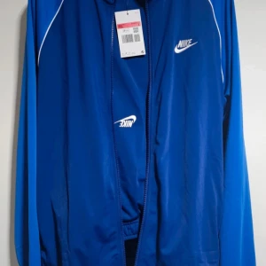 Nike Men's Sportswear Essential Tracksuit - Lightweight fabric offers comfort Jacket: High collar, full-zip, side zipped pockets and long raglan sleeves with ribbed cuffs and hem Pants: Elastic waist with drawcord, side pockets and ribbed cuffs for a snug fit Regular fit Material composition: 100% Polyester Size: Larg Funktioner: Andningsbar