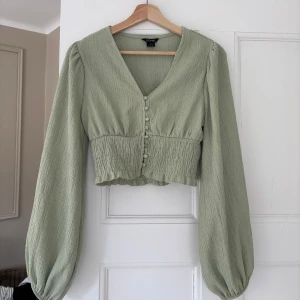 Grön blus från Monki - Säljer en stilren grön blus från Monki med långa ärmar och knappar framtill. 