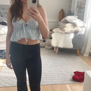 Blommig blå topp från NLY Trend - Säljer en söt blommig blå topp köpt på Nelly/NLY Trend. Toppen har smala axelband och en knytning framtill. Den är croppad med volangdetaljer och har ett fint blommönster i vitt. Säljer för att jag inte gillar den stilen på kläder längre. 