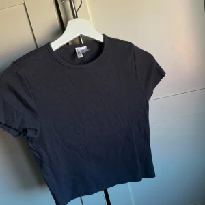 Svart ribbad t-shirt - Säljer en stilren svart ribbad t-shirt med korta ärmar. Perfekt för en avslappnad look. Passar bra till jeans eller kjol.