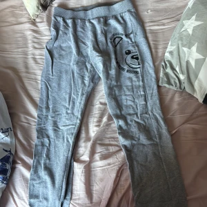 Grå mjukisbyxor från Moschino - Snygga grå mjukisbyxor från Moschino med ett coolt björntryck på sidan. Byxorna har en elastisk midja och en bakficka. Perfekta för en avslappnad stil. Priset kan diskuteras 