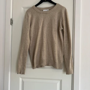 Beige stickad tröja från Vila - Säljer en mysig beige stickad tröja med rund halsringning. Tröjan har långa ärmar och ribbade muddar vid ärmslut och nederkant. Perfekt för kyliga dagar!