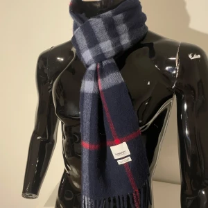 Marinblå halsduk från Burberry - Snygg och klassisk rutig halsduk från Burberry i marinblått med röda och ljusa ränder. Perfekt för att få en stilrent outfit under vintern och våren . Tillverkad i mjukt material för extra komfort. Smält andvänt och i toppskick , kom med prisförslag, vid snabb affär släpper jag den för billigare:)