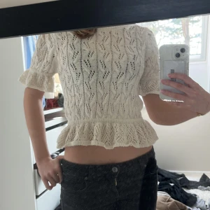 Vit stickad topp med volangdetalj - Säljer en söt vit stickad topp med korta ärmar och volangdetalj i nederkant. Passar bra till både jeans och kjol. Är i storlek M men passar xs/s