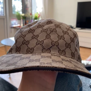 Beige keps från Gucci - Snygg beige keps från Gucci med det klassiska GG-mönstret i brunt. Kepsen har en justerbar rem baktill och detaljer i rött och grönt på sidorna. Perfekt för att ge din outfit en lyxig touch. Lappen är borta o kepsen är mjuk därför säljer jag den för 899