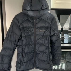 Svart dunjacka från Peak Performance - Säljer en svart dunjacka från Peak Performance med huva och dragkedja. Jackan är perfekt för en stilig look där den har en stilren design med Pertex Quantum-material för extra hållbarhet. Pris kan diskuteras!