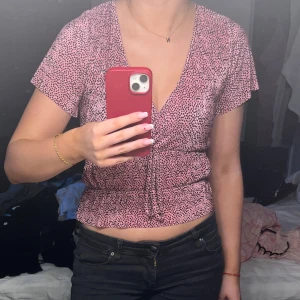 Rosa prickig omlottopp - Säljer en rosa omlottopp med små svarta prickar. Toppen har korta ärmar och är v-ringad. I storlek S❣️