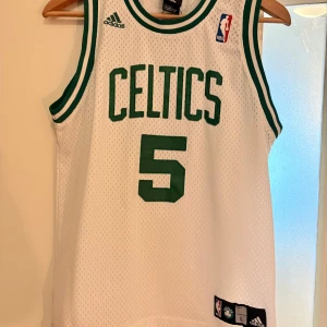 Vit Celtics basketlinne från Adidas - Säljer ett klassiskt vitt Celtics basketlinne från Adidas med gröna detaljer. Tröjan har nummer 5 och namnet Garnett på ryggen. Perfekt för basketfans som vill visa sitt stöd för laget. 🏀