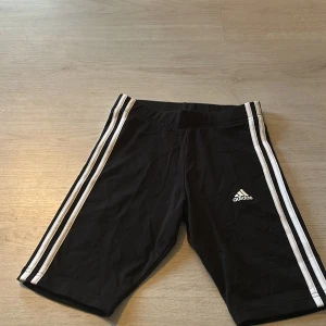 Svarta shorts från Adidas - Säljer ett par svarta shorts från Adidas med de klassiska tre vita ränderna längs sidorna. Perfekta för träning eller avslappnade dagar. Tillverkade i ett lätt och bekvämt material. Dom är äkta. Priset är inte satt öppen för alla förslag.