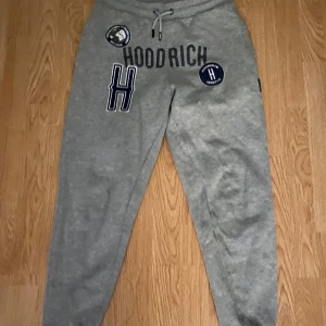 Grå mjukisbyxor från Hoodrich - Snygga grå mjukisbyxor från Hoodrich med tryck och broderade detaljer. Byxorna har en bekväm passform med snörning i midjan och elastiska muddar vid bensluten. Perfekta för en avslappnad stil.