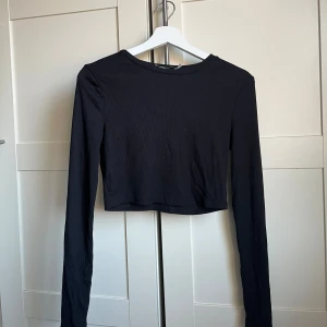 Svart ribbad croppad topp - Säljer en stilren svart ribbad croppad topp med långa ärmar. Perfekt för en trendig look. Passar bra till både jeans och kjol.