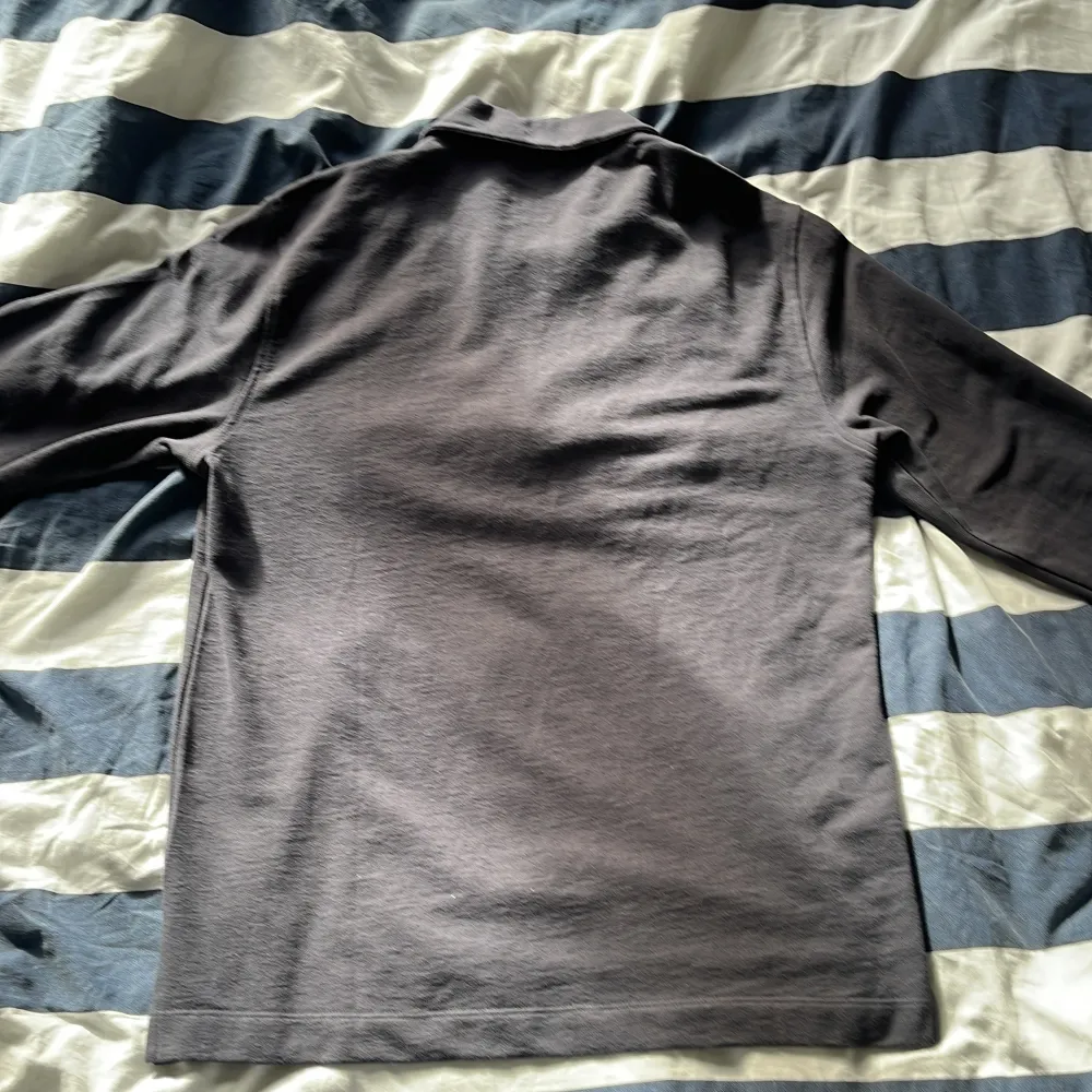 Snygg svart långärmad pikétröja från Dobber med dragkedja vid halsen. Perfekt för en stilren och avslappnad look. Tröjan har en klassisk krage och är tillverkad i ett bekvämt material.. Neuletakit & Villapaidat.