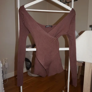 Brun omlottop - Säljer en ribbad brun omlottop med djup v-ringning och lång ärm. Tröjan har en figurnära passform och är tillverkad i stretchigt material som sitter snyggt på kroppen. Perfekt för dig som gillar trendiga och stilrena plagg.