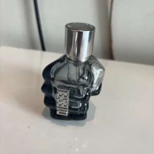 Diesel Only The Brave parfym (tom flaska) - Cool parfymflaska från Diesel formad som en knytnäve i mörkgrått glas med silvrig metallogo och lock. Flaskan har en unik och edgy design som sticker ut i badrumshyllan. Perfekt för dig som gillar statement-detaljer och modern stil.