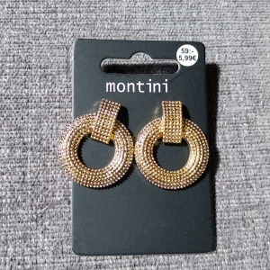 Guldiga statementörhängen Montini - Runda, chunky örhängen i guld från Montini. De har en cool texturerad yta med små pärlliknande detaljer som ger extra bling. Perfekta för att lyfta vilken outfit som helst med sin trendiga och iögonfallande design.