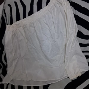Vit offshoulder blus med lång ärm - Säljer en vit offshoulder blus med långa ärmar och resår upptill. Blusen har en luftig och avslappnad passform, perfekt för en trendig och chill look. Materialet känns lätt och passar bra till både jeans och kjol. Använd endast en gång 