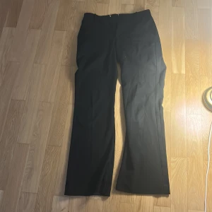 Svarta kostymbyxor från Lindex - Svarta kostymbyxor från Lindex i klassisk rak modell. Byxorna har midjehällor, diskret dragkedja och är tillverkade i ett mjukt tyg. Köpta för 699kr säljer för 429kr