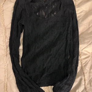 Svart stickad långärmad tröja - Svart stickad tröja med lång ärm och rundad halsringning. Tröjan har ett genombrutet, mönstrat stickat material som ger en snygg och luftig känsla. Perfekt att styla med jeans eller kjol för en chill look.