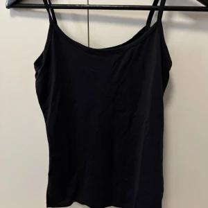 Svart linnetopp från Zara - Enkel och stilren svart linnetopp från Zara med smala axelband. Toppen är figurnära och har en klassisk, rundad halsringning. Perfekt att matcha med jeans eller kjol för en clean look.