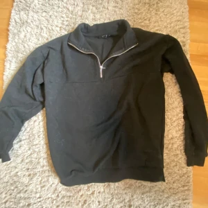 Svart half zip sweatshirt - Svart sweatshirt från SMOG i relaxed fit med halv dragkedja framtill. Tröjan har hög krage och långa ärmar, perfekt för lager-på-lager. Mjuk och skön känsla, passar till chill eller när du vill vara bekväm.