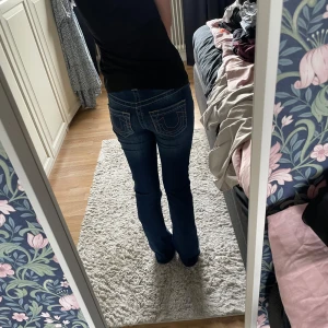 True Religion blå bootcut jeans mod waist  - Snygga blå jeans från True Religion med klassiska kontrastsömmar och ikoniska bakfickor med broderad logga. Modellen har bootcut-ben och låg midja. Jeansen är tillverkade i kraftigt denim och har en autentisk tvättad look. Dem är uppsydda så dem passar mig som är ca 150cm