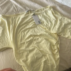 Ljusgul offshoulder T-shirt 157 XS - Supersöt ljusgul offshoulder T-shirt från 157 i storlek XS. Klänningen är enkel och stilren med mjukt material och passar perfekt för varma dagar. Den har en kort längd och är ärmlös, vilket ger en fräsch och somrig vibe.